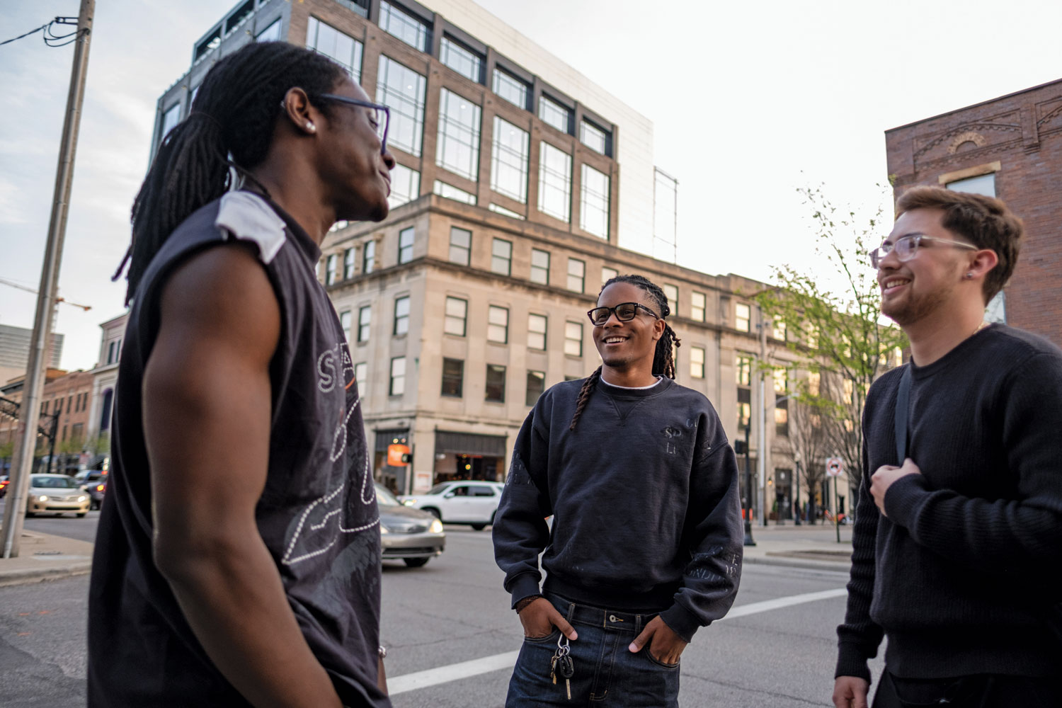 Justen Turner and his friend and sometimes-colleague Tobias Zuniga-Shaw chat with an acquaintance they ran into in the Short North. Tobias is a young man who looks about the same age as Justen. They both wear dark sweatshirts, dark blue jeans and thick-rimmed glasses.