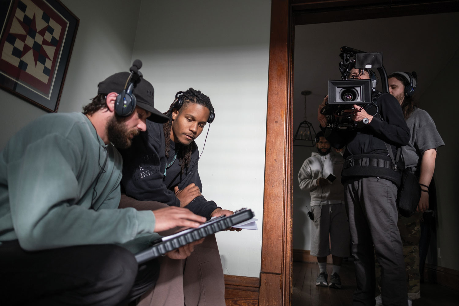 As a camera operator stands in a doorway filming into a room, Justen huddles with another crew member discussing a production point.  