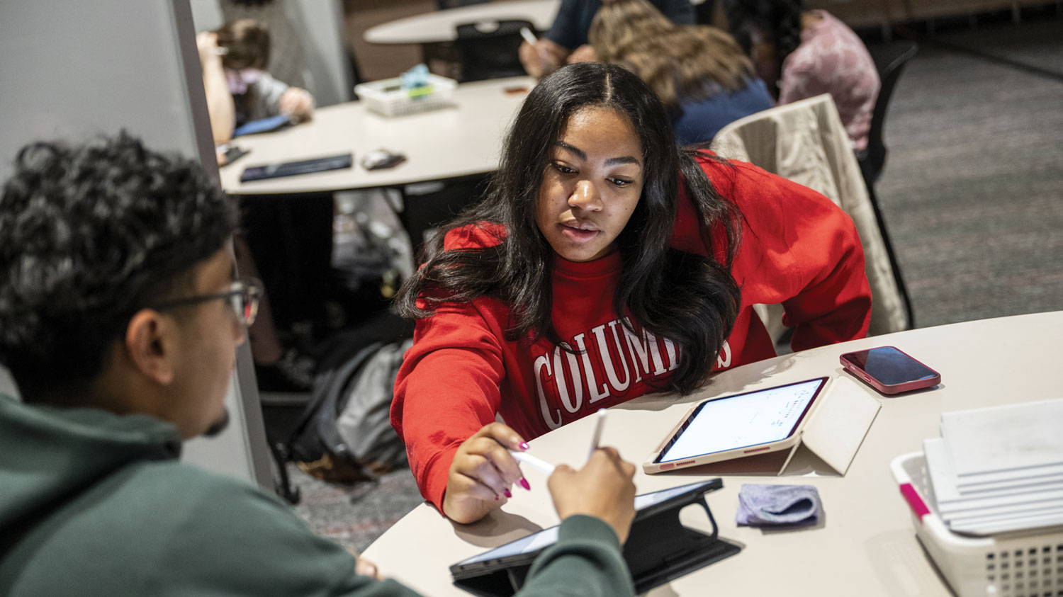 Two students discuss a point as they both point to a tablet computer.