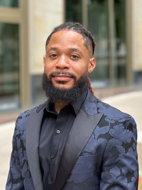 Terron Banner poses for a professional portrait in front of Urban Arts Space. He wears a blue-flowered blazer.