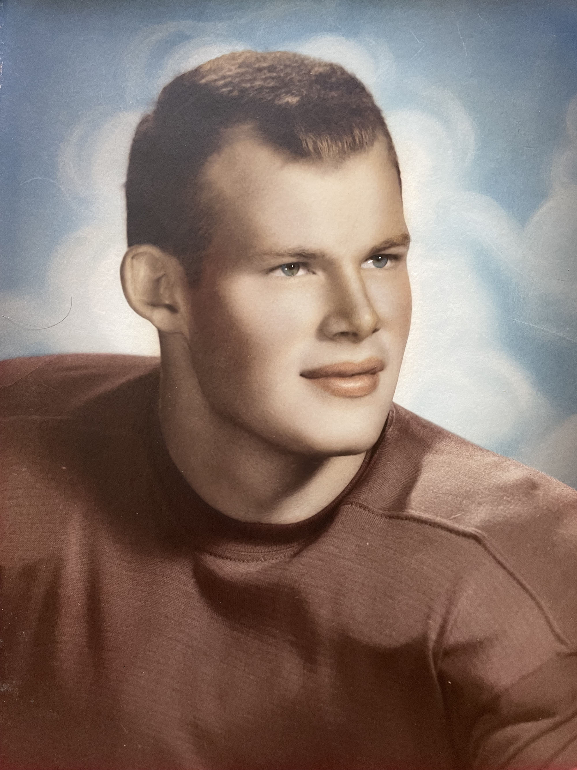 A handsome young man gazes off to his left in an official headshot photo from the 1960 football season. He has closely cropped hair, blue eyes and a slight smile.