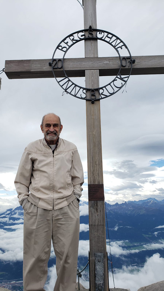 An older man with a friendly smile poses with his hands in his pockets while on Bergsohn Innsbruck, while on a ski hill in Austria. 