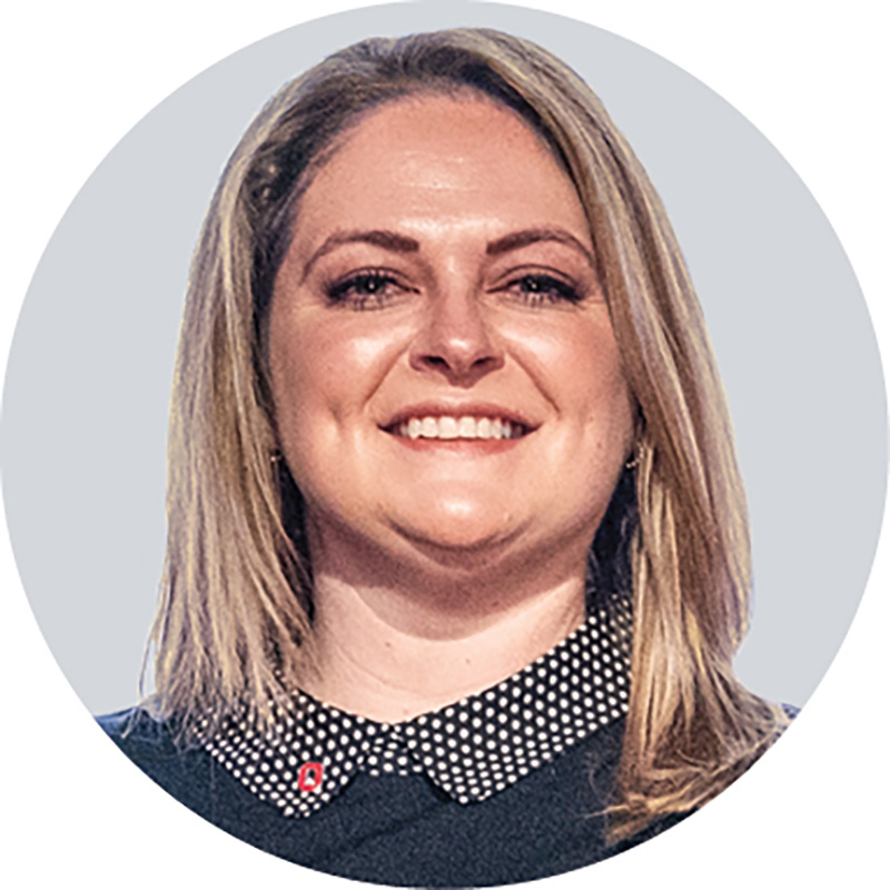Sara Gombash Lampe smiles after getting her award. This headshot shows she is a blond woman wearing a dress with a cute polka-dot collar peaking out. Her Block O pin is on her collar.