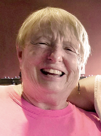 A smiling woman with short hair looks down toward the camera. She's wearing a pink T-shirt