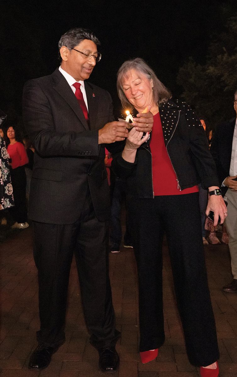 Molly Ranz Calhoun, head of the alumni association, laughs as she leans toward Ohio State President Ravi Bellamkonda to light her candle from one he holds. These are slim, about five inches long and have cardboard circles to keep wax from dripping on their hands. Bellamkonda cups his hand around the flame as he smiles and focuses.