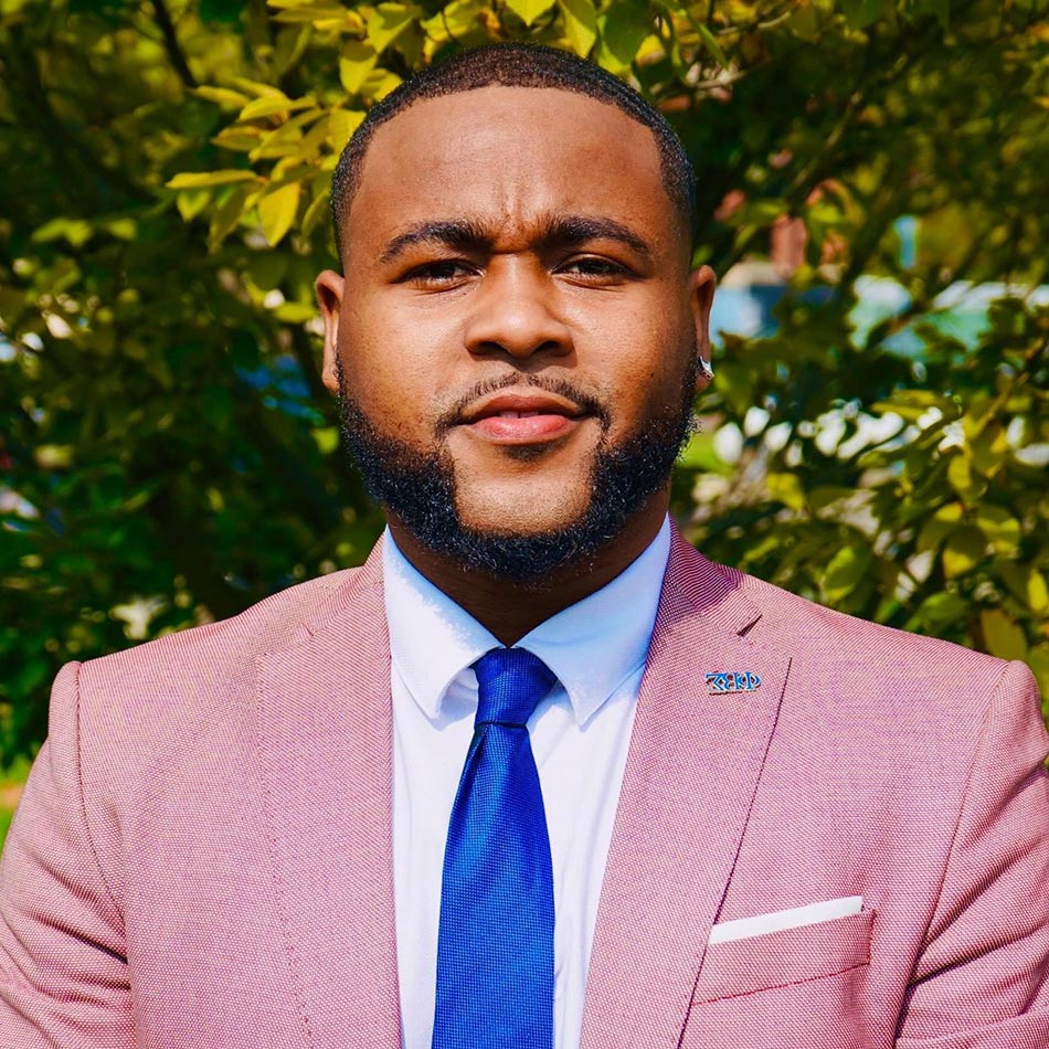 portrait of Demondre Peak wearing a salmon colored suit and blue tie