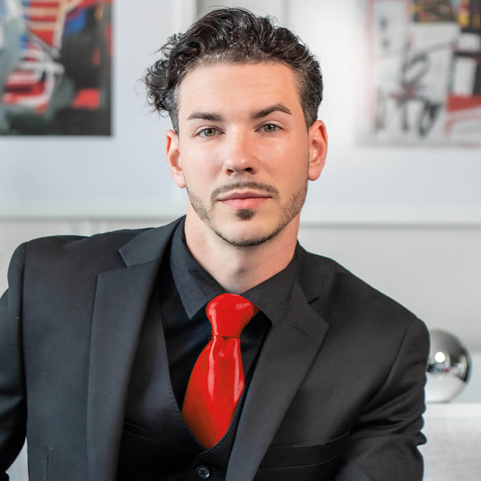 portrait of Mikey Gundich wearing a black suit with a red tie