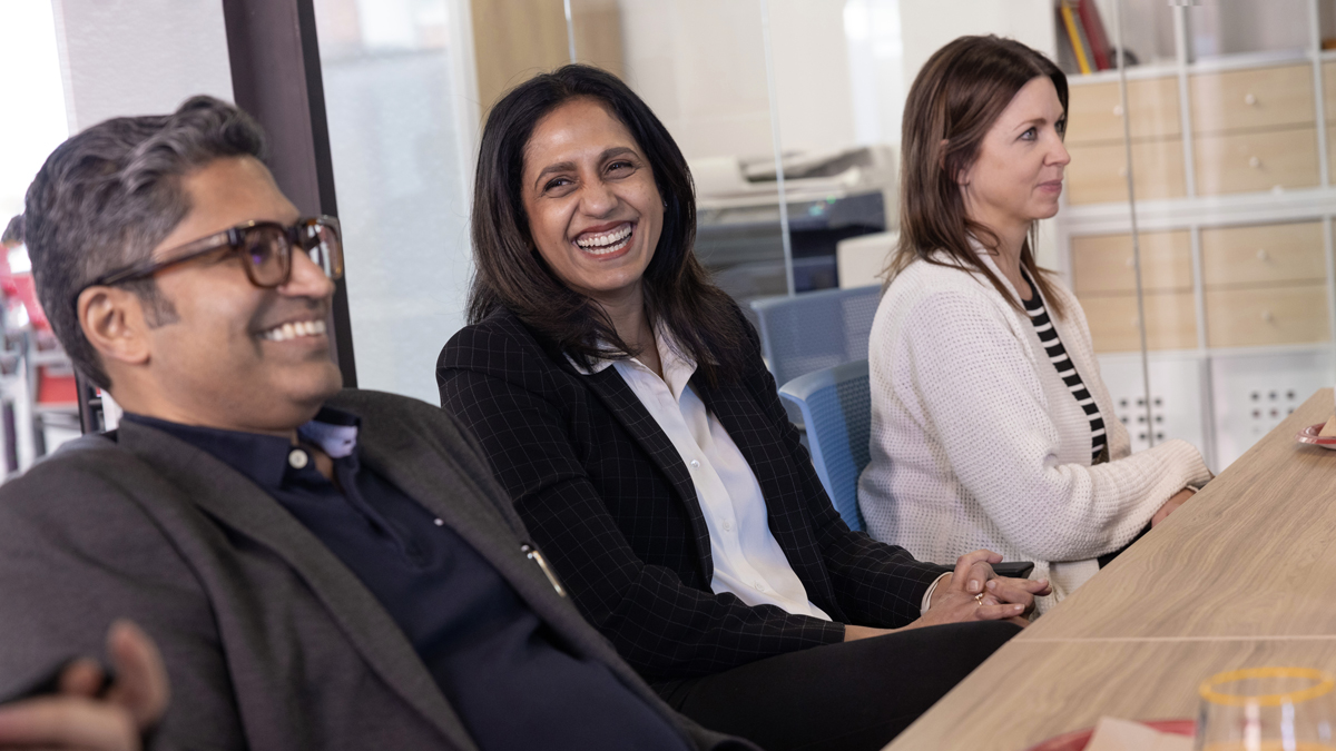 Bharat, Bhakti and a colleague sit at a meeting room table laughing.