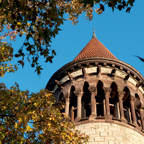 The spire atop Orton Hall framed by trees and cloudless blue skies.