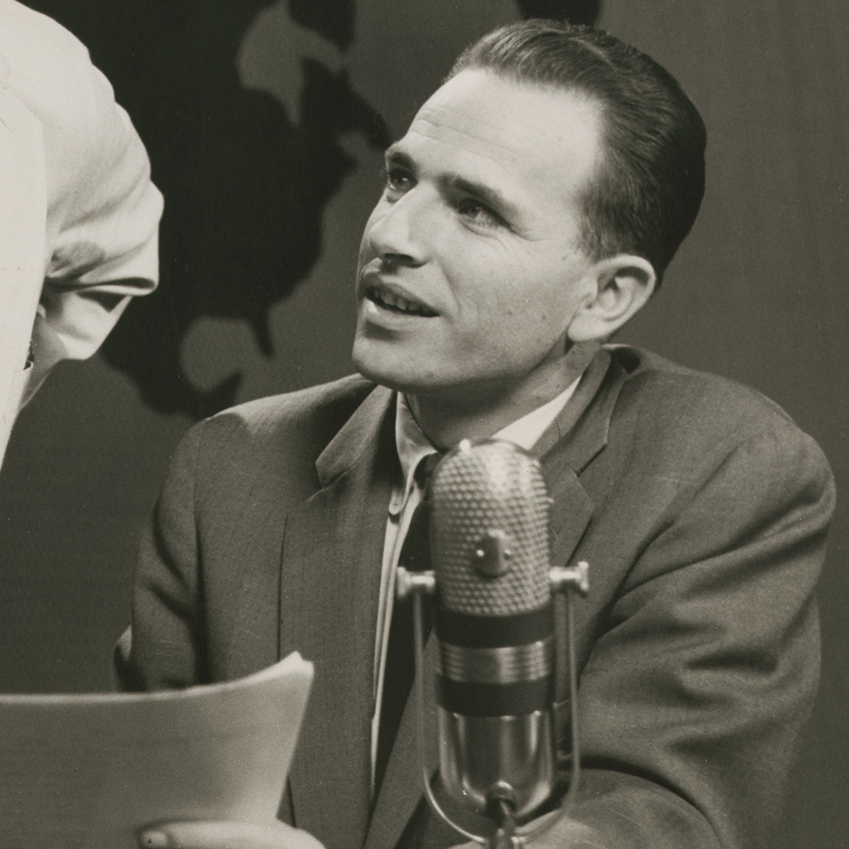 Vintage black & white photo of a young man in front of a radio broadcast microphone