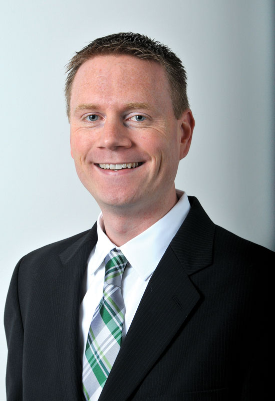 Paul Reiter grins as he poses for an official portrait. He's a white man wearing a suit and plaid tie.