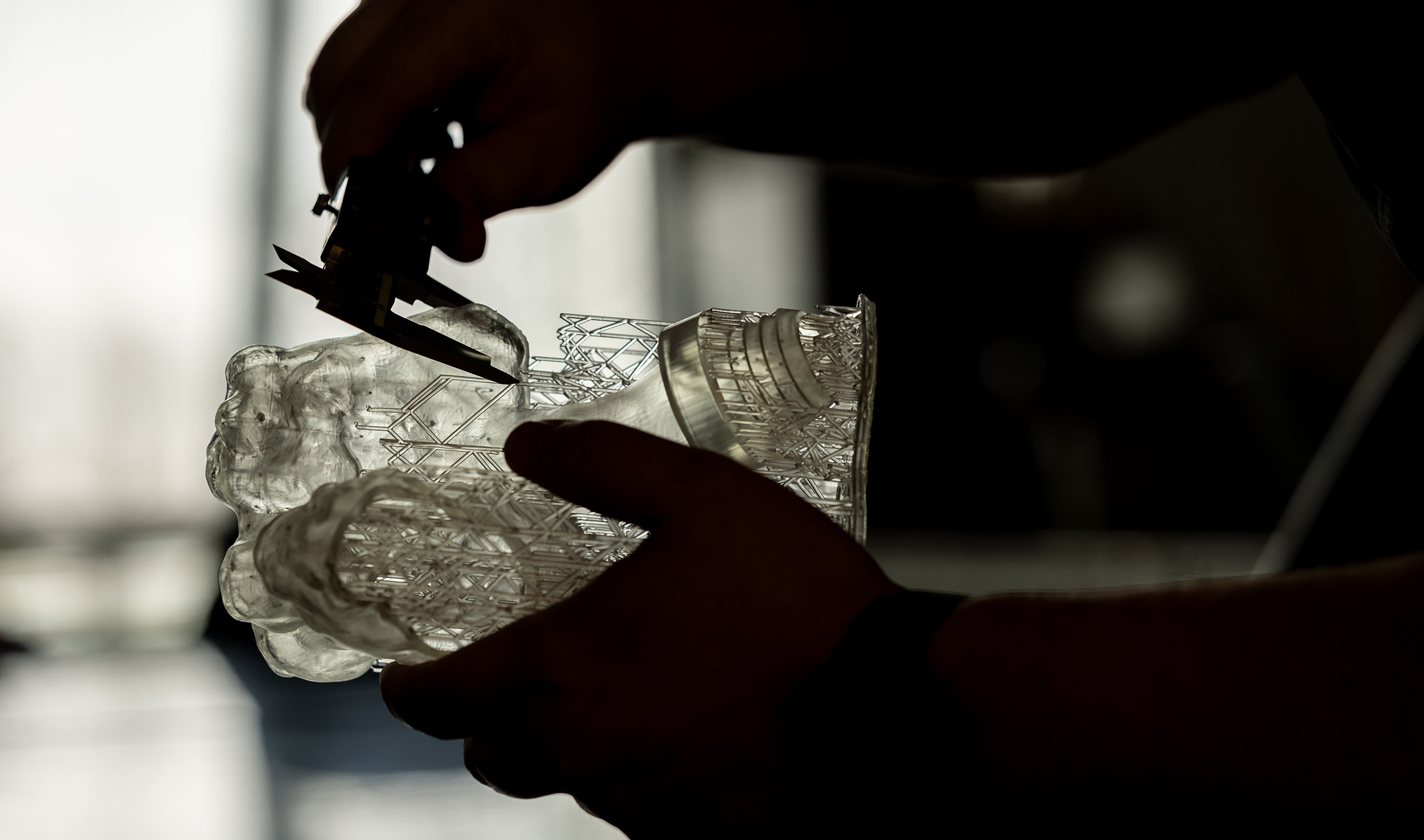 light shines through a transparent model that a silhouetted person holds in their left hand.  In their right is a caliper they're using to measure part of it.
