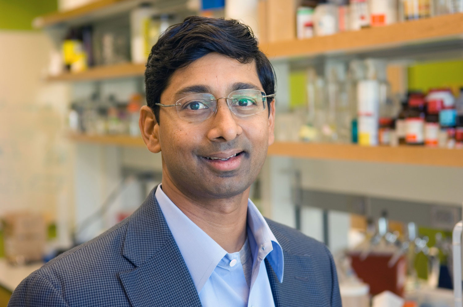 A much younger Bellamkonda wears a suit and smiles while standing in a laboratory.