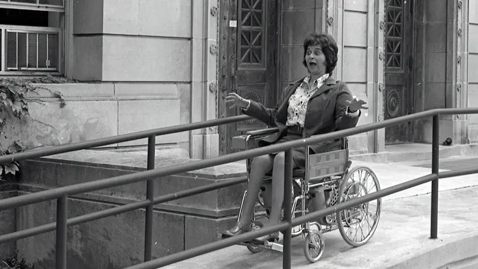 Black and white archival photo of Julie Cochran in her wheelchair using a university ramp for the first time.