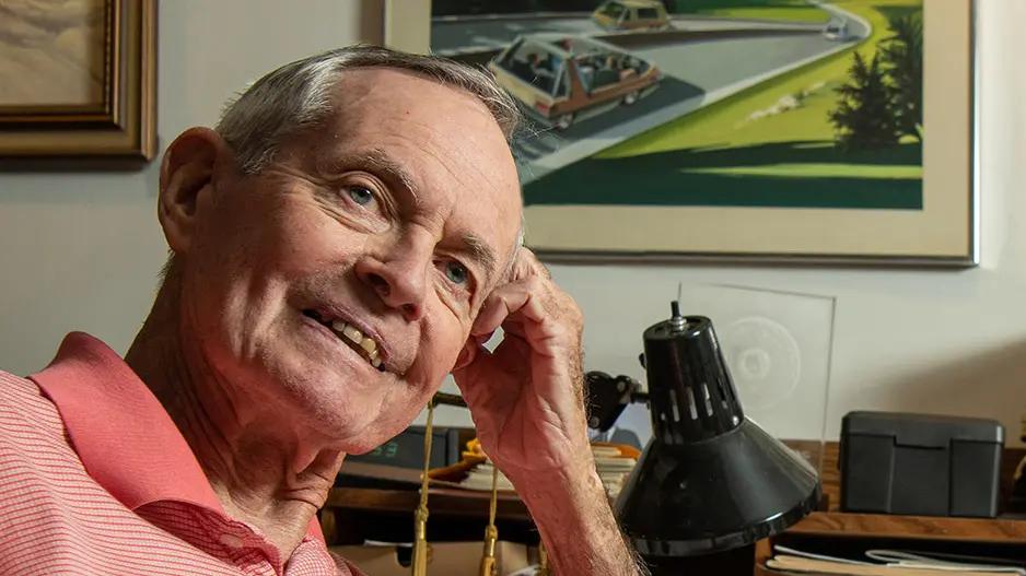 Portrait of Robert Fenton wearing a pink and white striped polo, seated in his office. 
