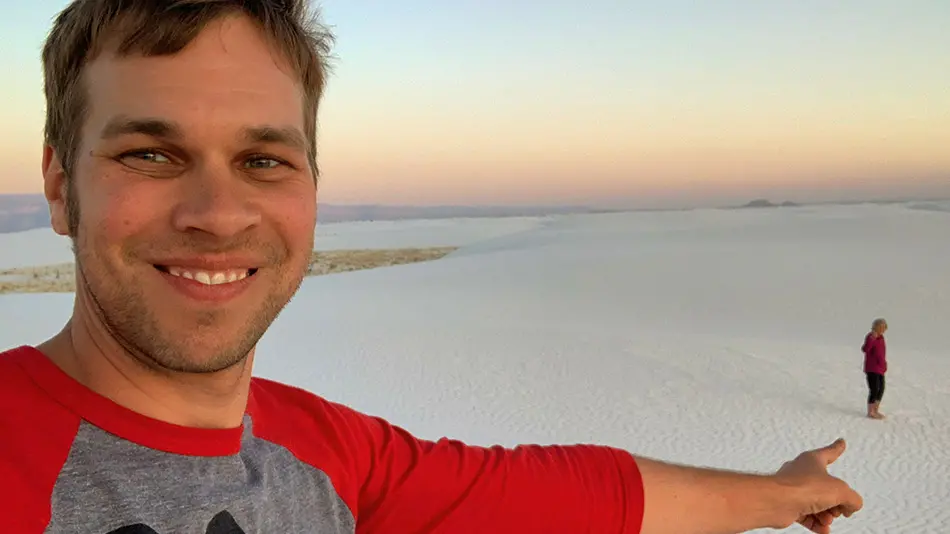 Brad is standing in the foreground on a white sand beach. He is pointing to Grandma Joy, who standing at a far distance from Brad.