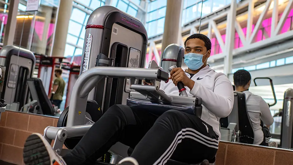 Ronnie Tate is seated on a piece of exercise equipment with a large mirrored wall behind him.