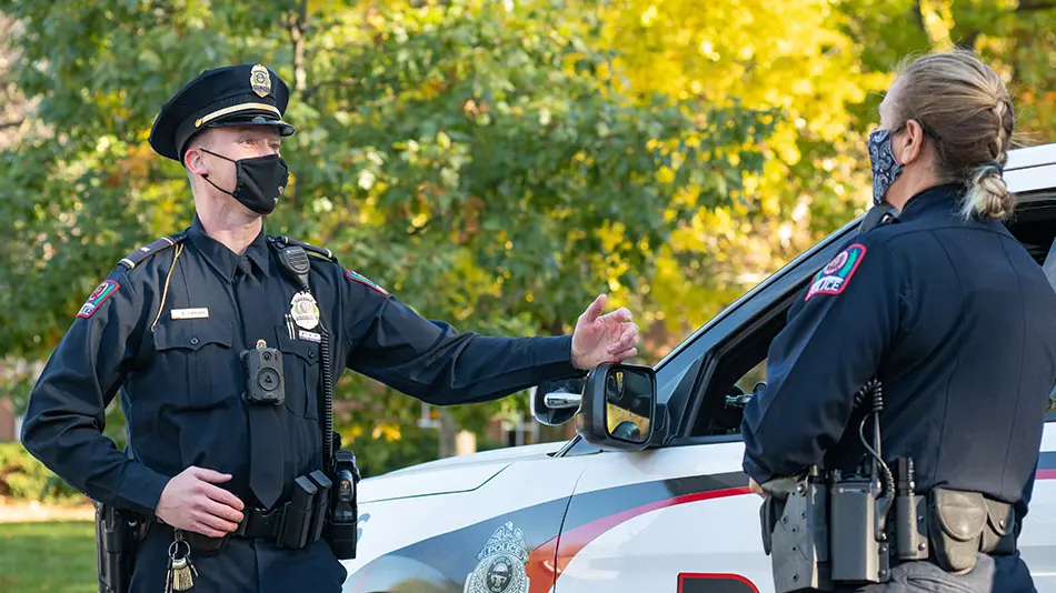 Brandon Yankanin and Regina Shoopman are standing in uniform next to a police car having a discussion.