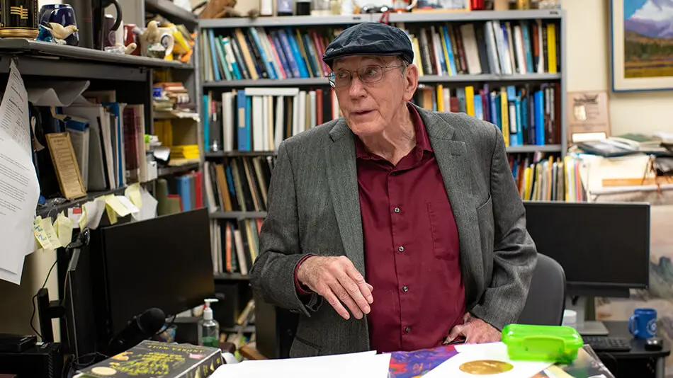 man talks in a an office chock-full of books and papers