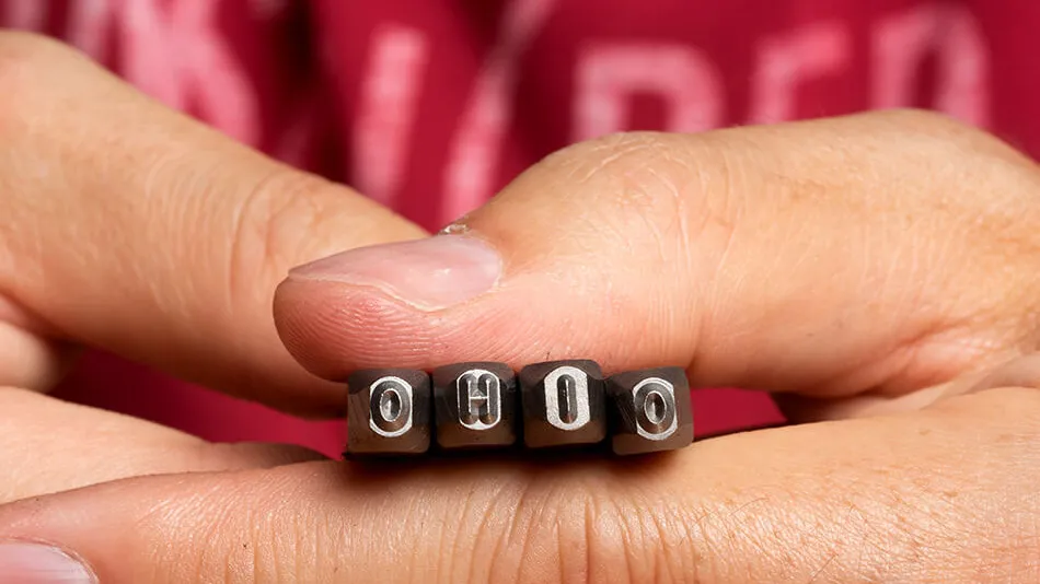 Hands holding stamping tools that spell "Ohio"