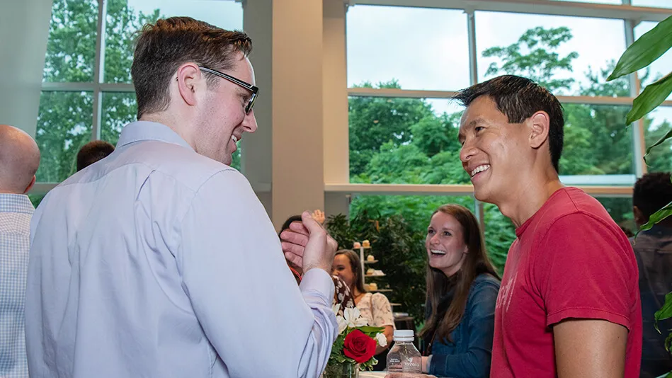 Photo of Chris Pan in red t-shirt taking to white man in long sleeve dress shirt. 