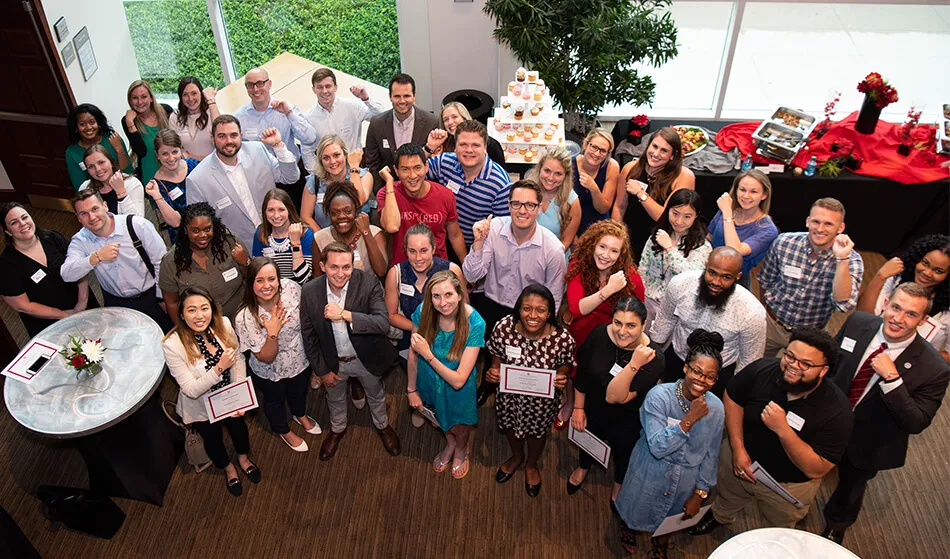 Photo taken on ladder of young alumni group at an event posed in rows in front of buffet table