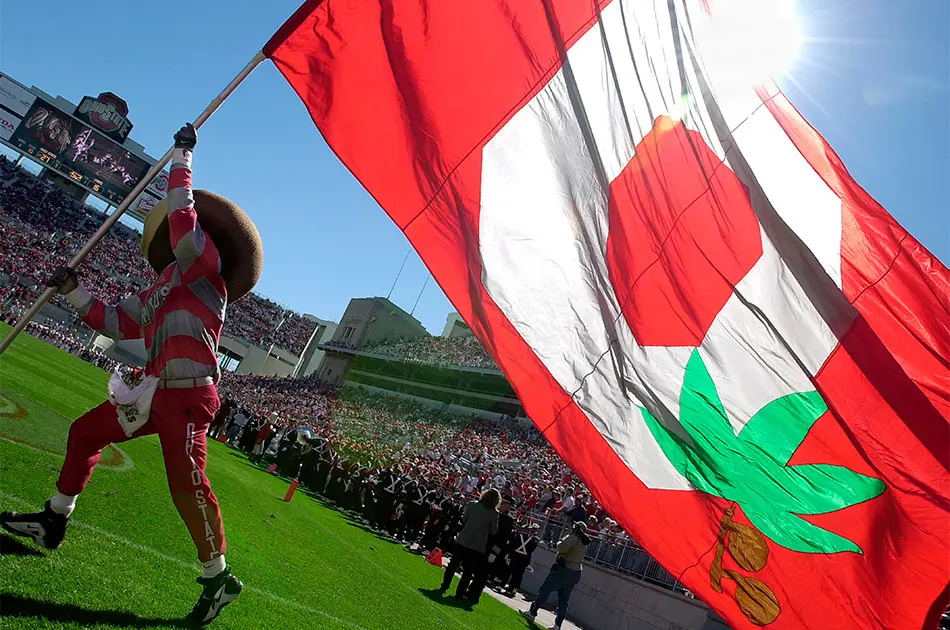 Brutus Buckeye running out onto the football field waving a block O flag