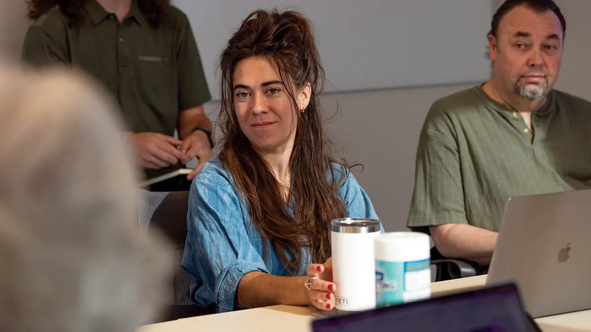 A white woman with long brown hair looks interested while listening in a meeting. 