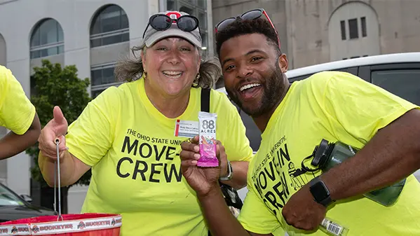 Molly poses next a young man. They are both wearing bright yellow shirts that say Move-In Crew as they volunteer to help students move into their campus rooms