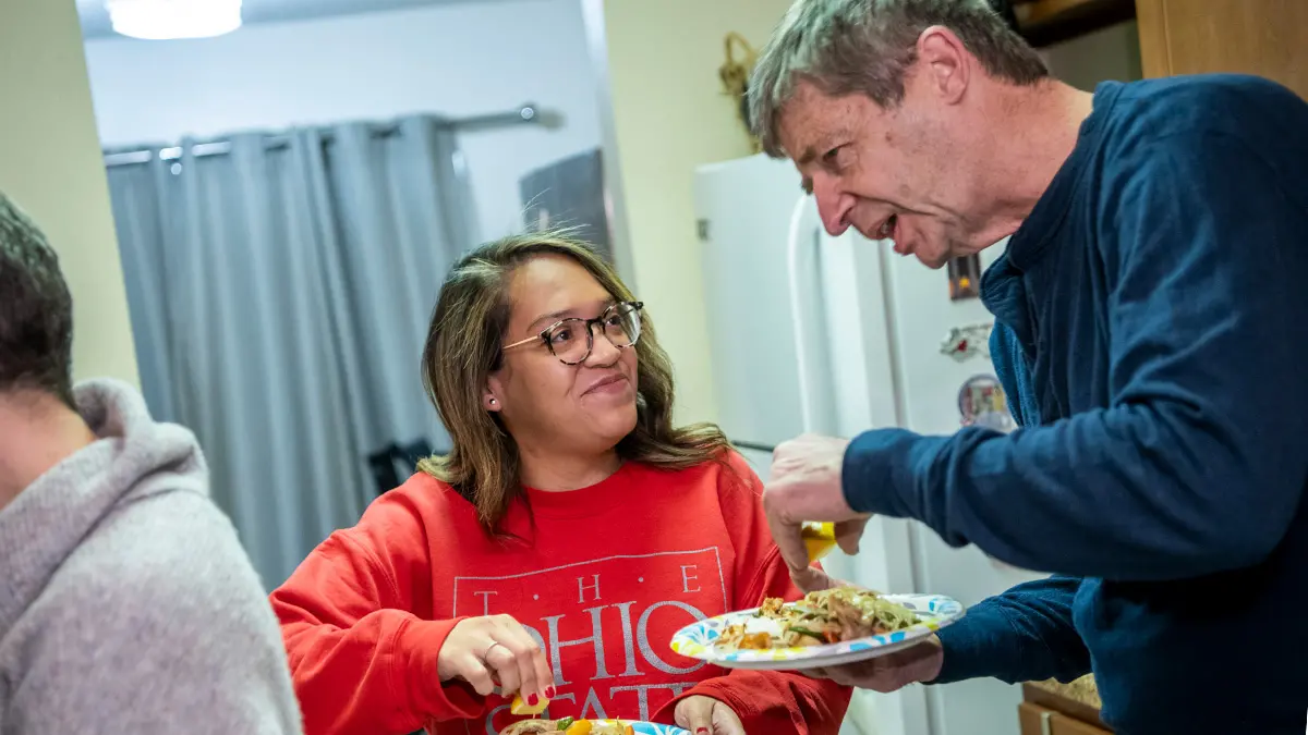 A young doctor smiles as an older man talks to her. They’re both holding paper plates with good-sized heaps of Filipino food.