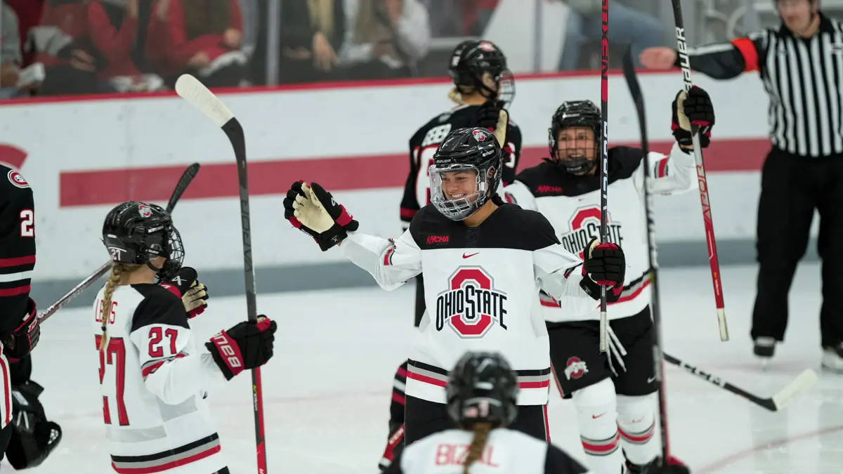 Hockey players on the ice celebrate and seem like they’re about to give one another high fives and hugs. They wear Ohio State uniforms.
