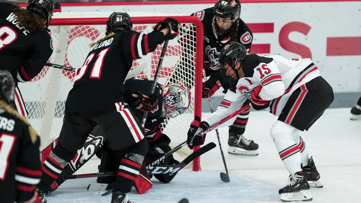 In an action photo taken during a game, an Ohio State player reaches with her stick for the puck right at the other team’s goal. The defending goalie squats, trying to stop the puck, and three more of her teammates are futilely moving to help.