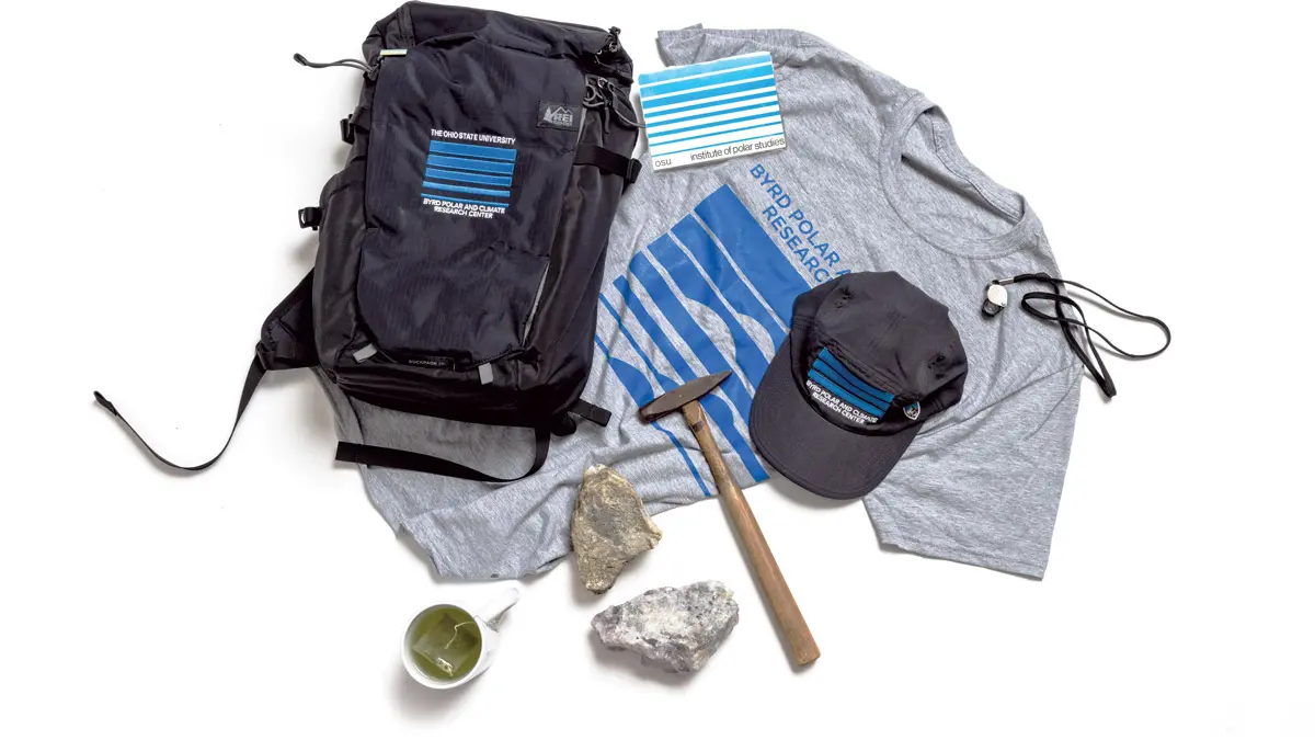 A T-shirt, backpack and baseball cap are each adorned with variations of a logo that is a rectangle of bars of blue with space between them. The bars vary in depth and are usually thicker at top. They could be seen as sky over a glacier or different layers of a glacier. Also shown are rocks, a hammer and a mug of tea.