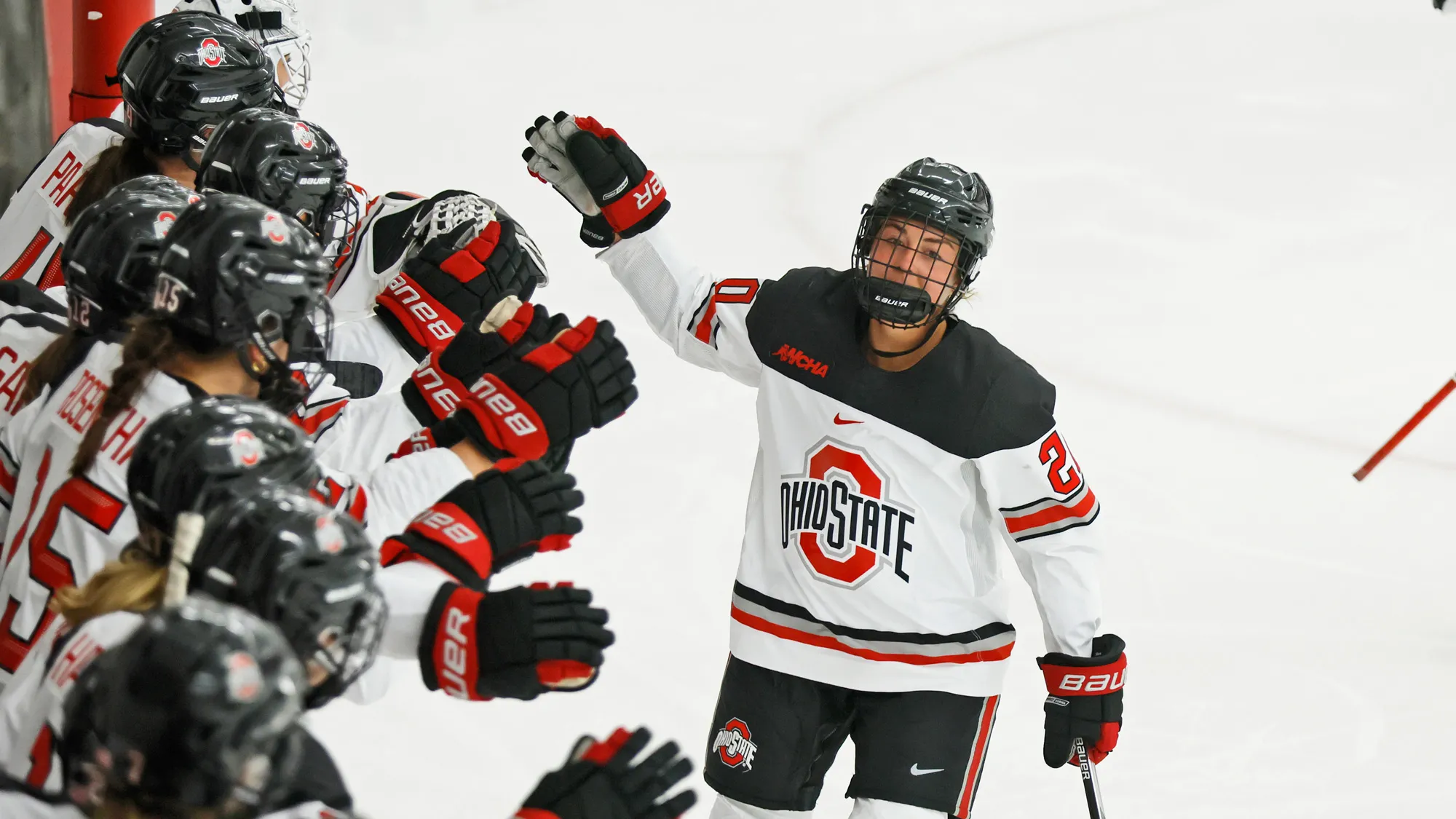In her game uniform and helmet, Makenna Webster skates along a line of her ice hockey teammates giving high fives. 