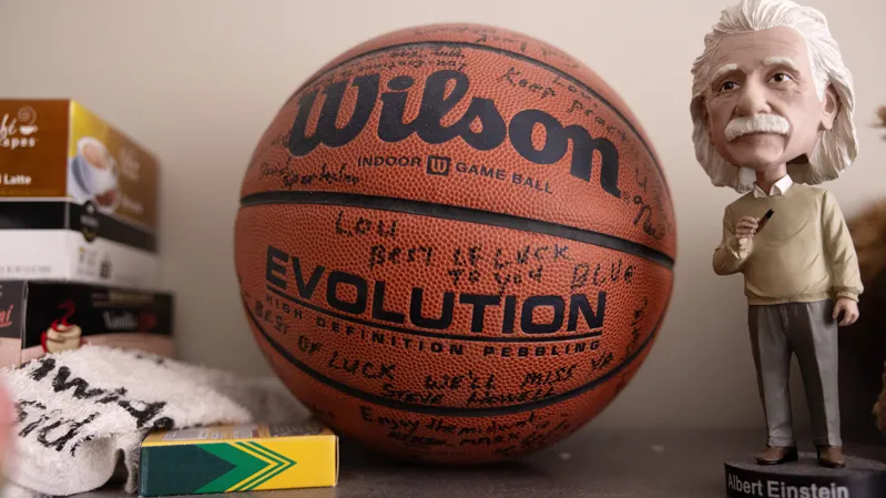 A bobble head doll of Albert Einstein sits next to a basketball signed by Lou DiMauro's old co-workers before he came to Ohio State. They're on top of a shelf, next to a stack of tea and crayons. 