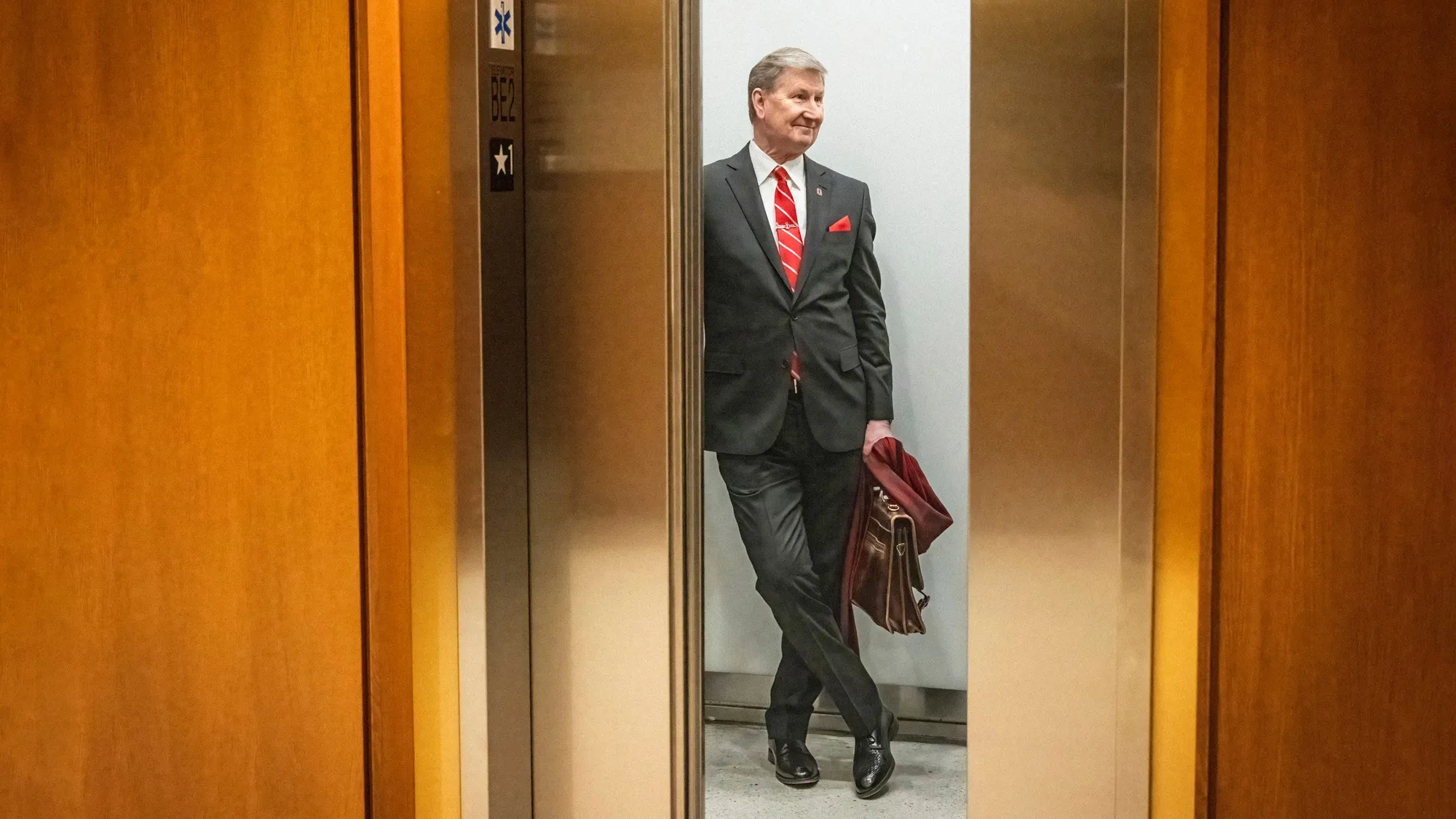 President Carter stands casually as brass-colored elevator doors close between him and the photographer. Carrying his scarf and work bag, Carter looks happy.