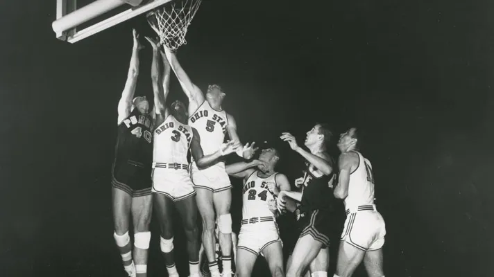 In a 1960 basketball game, three players jump high off the court to lay up and block a shot. Three more players on the ground box out opponents or prepare in case there’s the chance to rebound. Four of the six are Ohio State players—the others are from Purdue. Five of the six are white men; one Ohio State player is black. They’re all tall and think and focused on the ball.