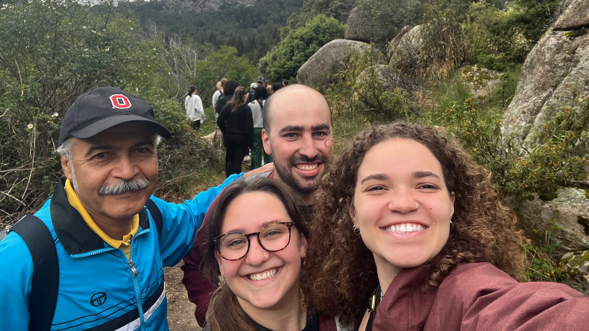 On a hiking trail, Ariana poses with three others two near her age and an older man wearing an Ohio State ballcap. They're all smiling like they're enjoying themselves.