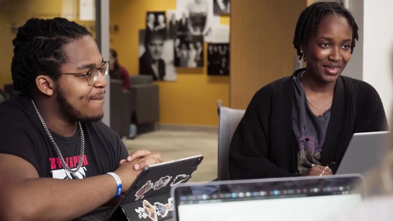 Two people work inside the Barnett Center at a table. Across from them sit more collaborators, but they're off screen.