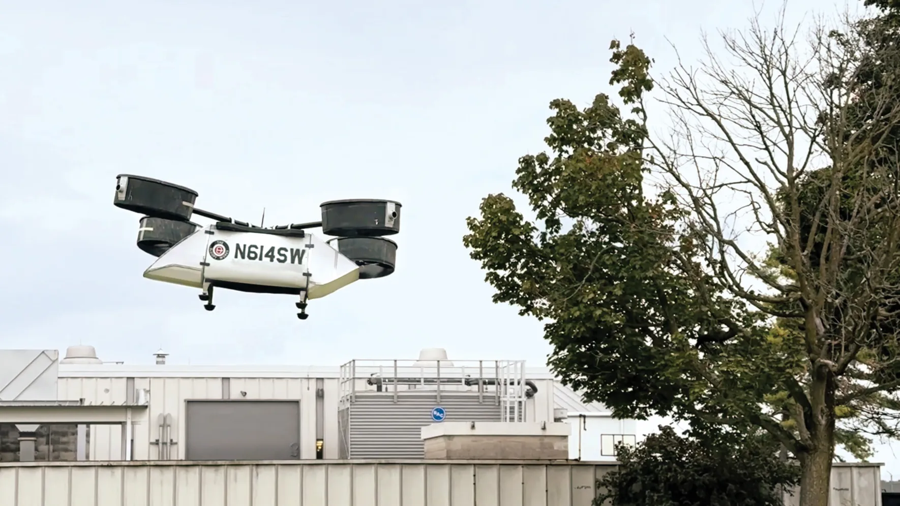 A model rescue drone created at Ohio State flies into the air. It has a large body to ferry people or supplies and 8 propellers enclosed in four cannisters, each at the end of a pole. Together, they're laid out as a helicopter's rotors would be.  
