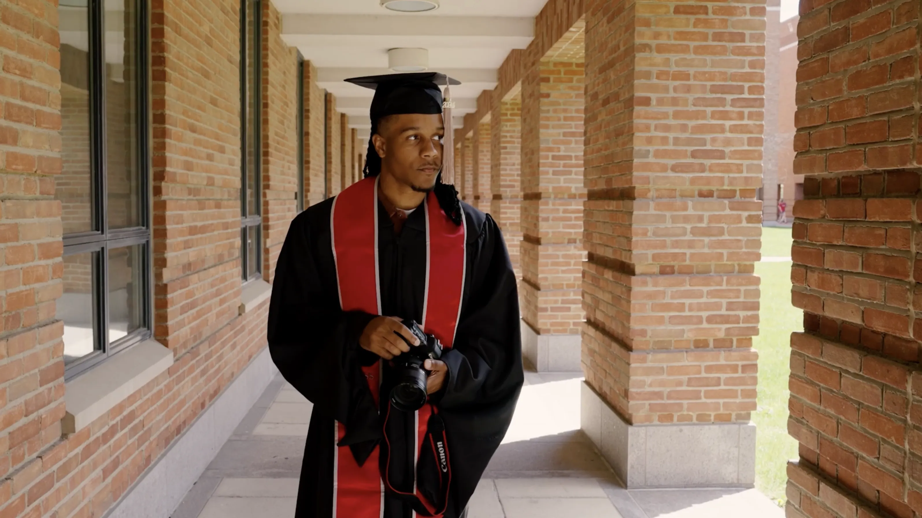Justen Turner, in cap and gown, walks through the portico outside Fisher College of Business.