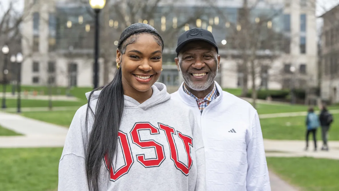 Faith and Keith Hunter smile as they pose on the Oval. Thompson Library is in the background. 