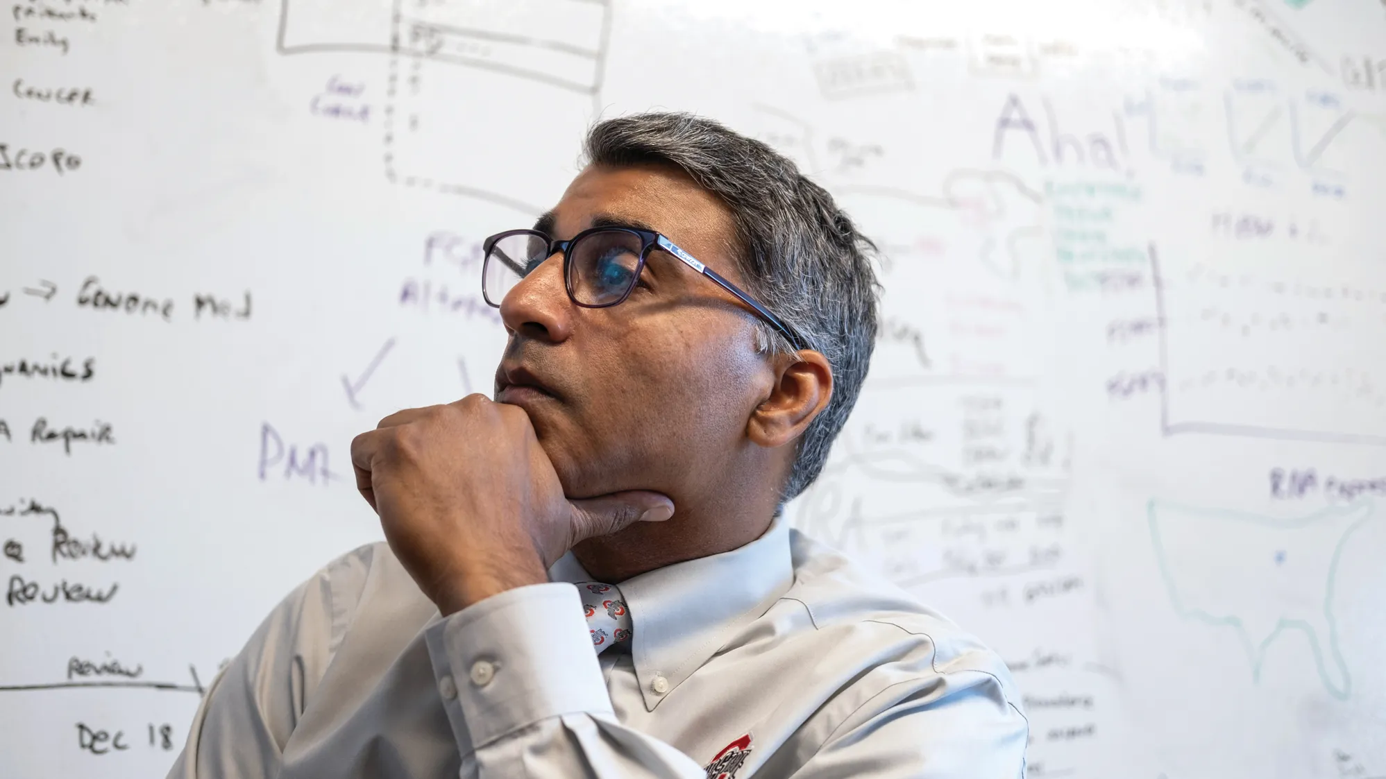 Sameek Roychowdhury listens to a remote patient during a meeting in his team's office. Behind him is a white board that has writing all over it.