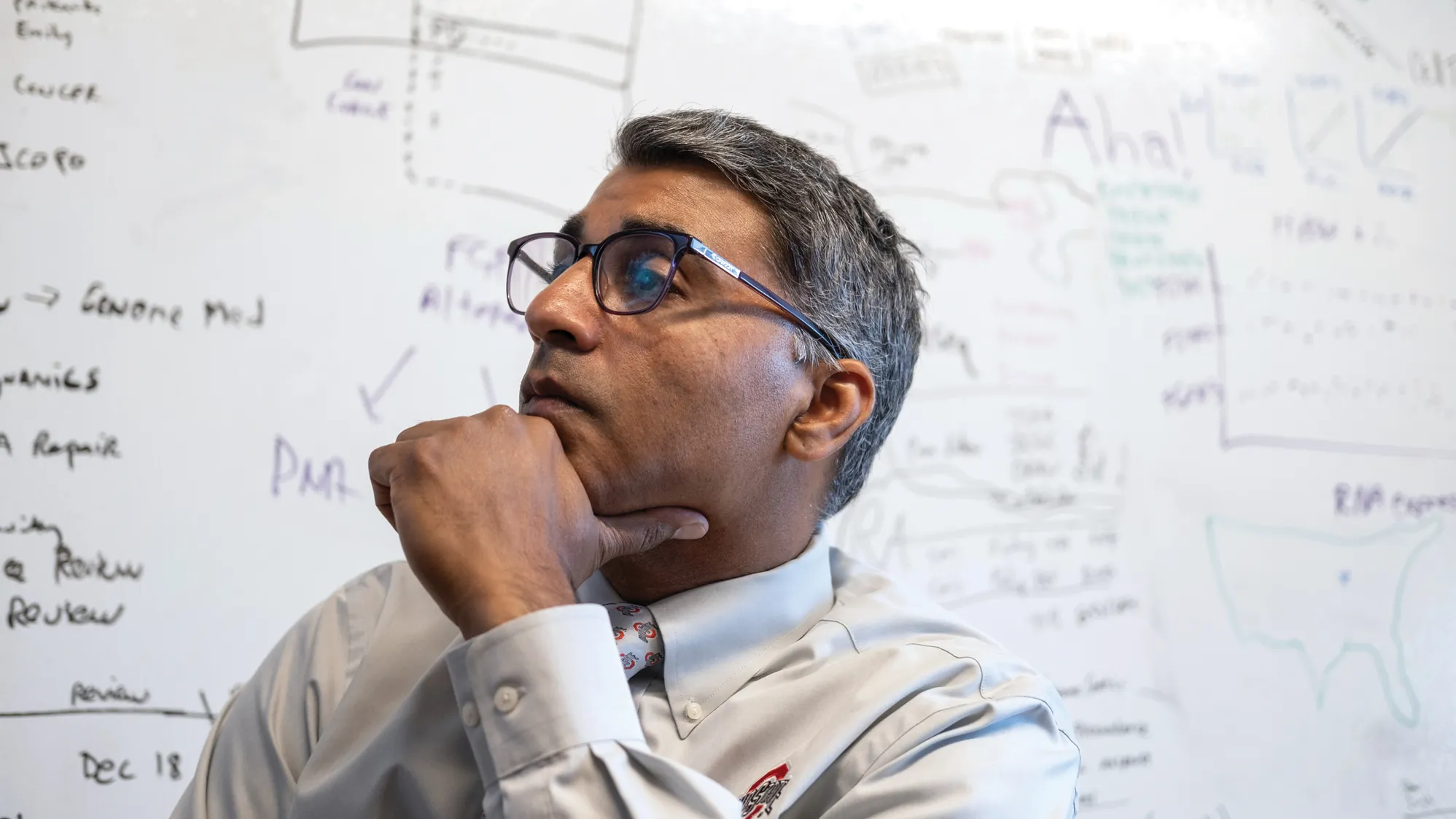 Sameek Roychowdhury listens to a remote patient during a meeting in his team's office. Behind him is a white board that has writing all over it.