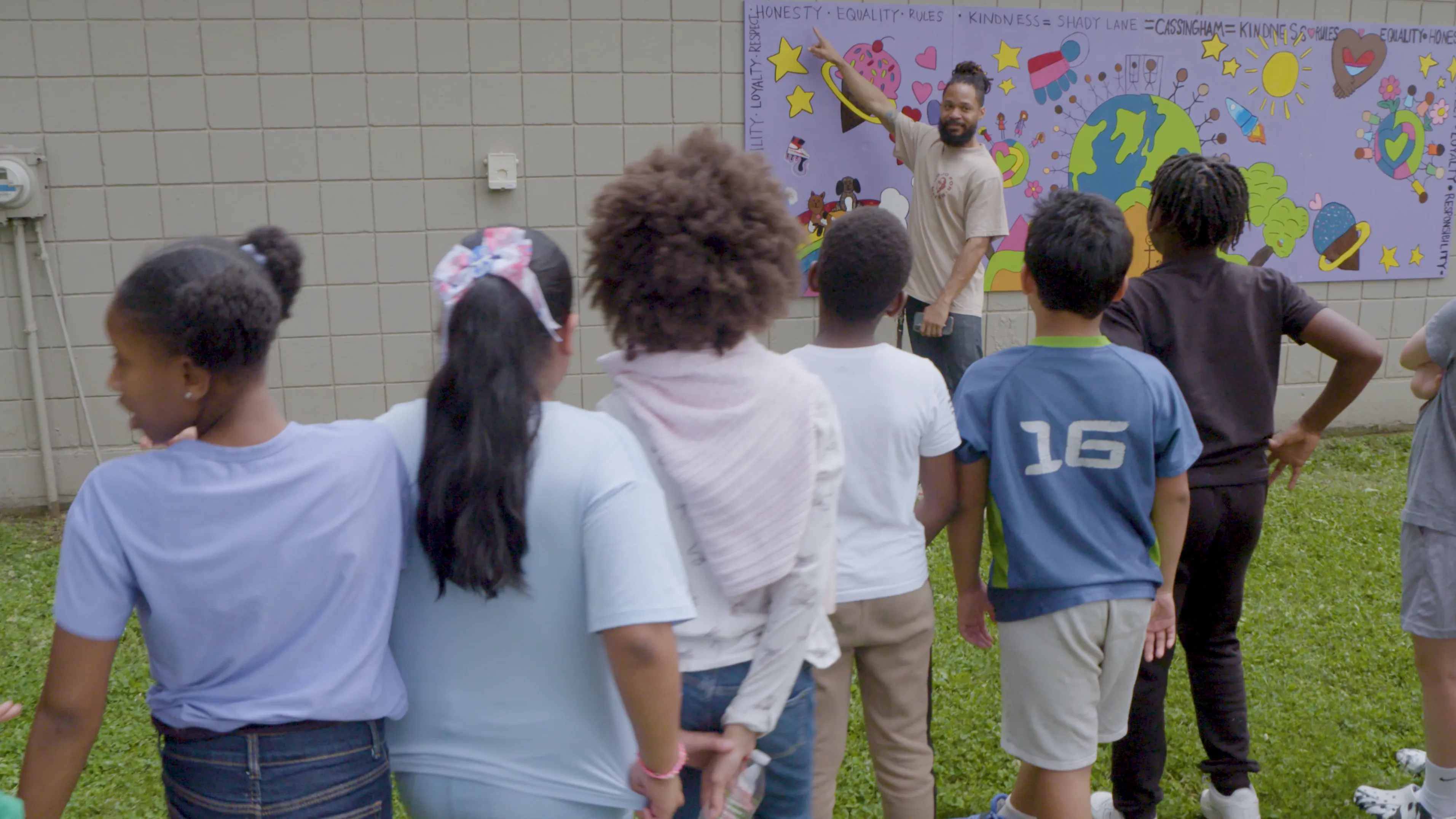 Terron Banner points to part of a mural, a word in the corner that says honesty, as kids line up in front of him. They're laughing and talking about the mural they made together.
