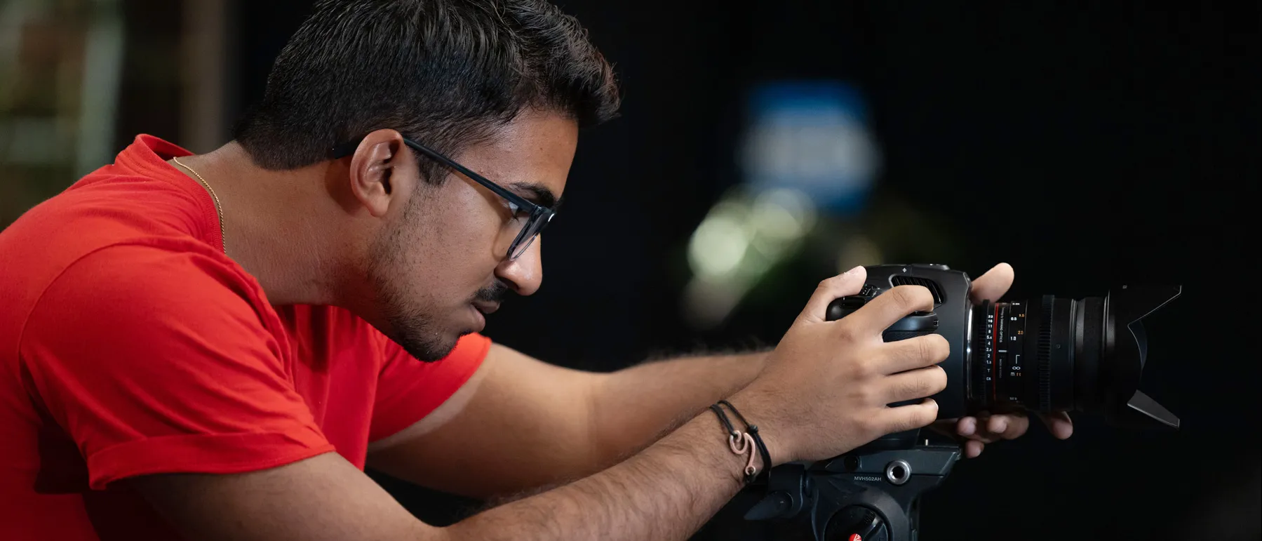 David Cassady, a young man with a neat haircut and wearing glasses, leans forward to focus on the screen of the camera he’s working. He’s shown from the side. Behind him, the room is dark as his class is exploring lighting effects in films.