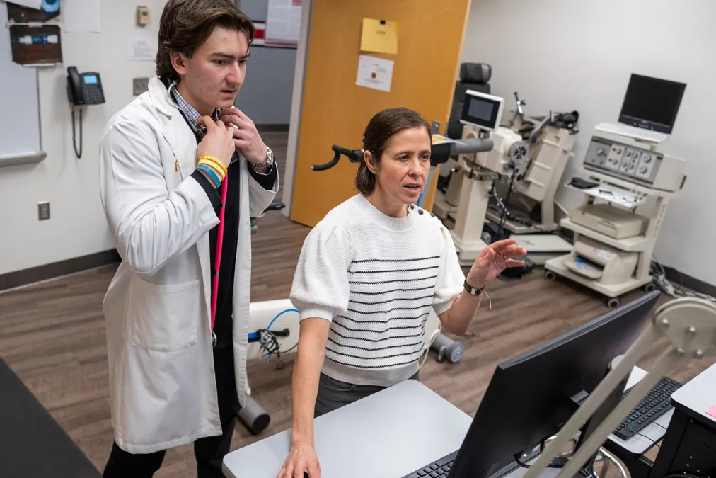 Carmen Swain and Anthony Dujmovic work together as they stand in from of a computer screen tracking test results as a person off camera exercises.