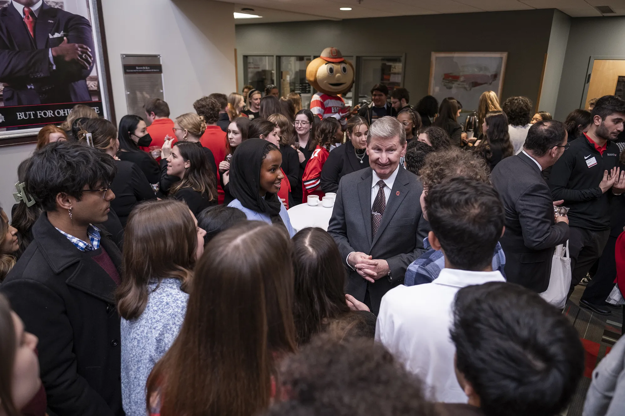 Standing in a crowd of students, President Carter chats with a couple as others wait their turn for conversation and selfies.