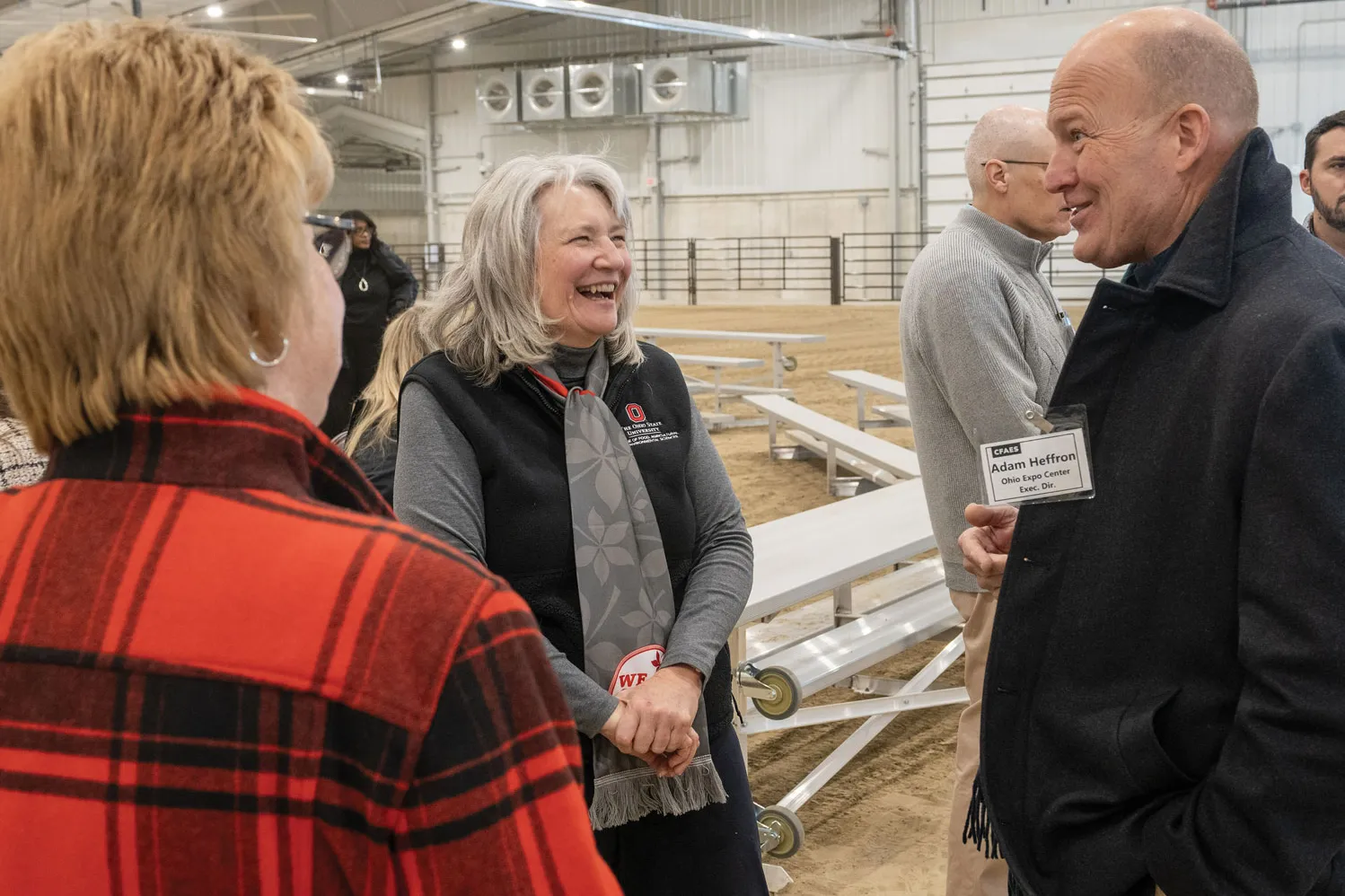 A woman laughs as she speaks with a man. Another woman faces them, her back is to the camera but it looks like she's smiling.