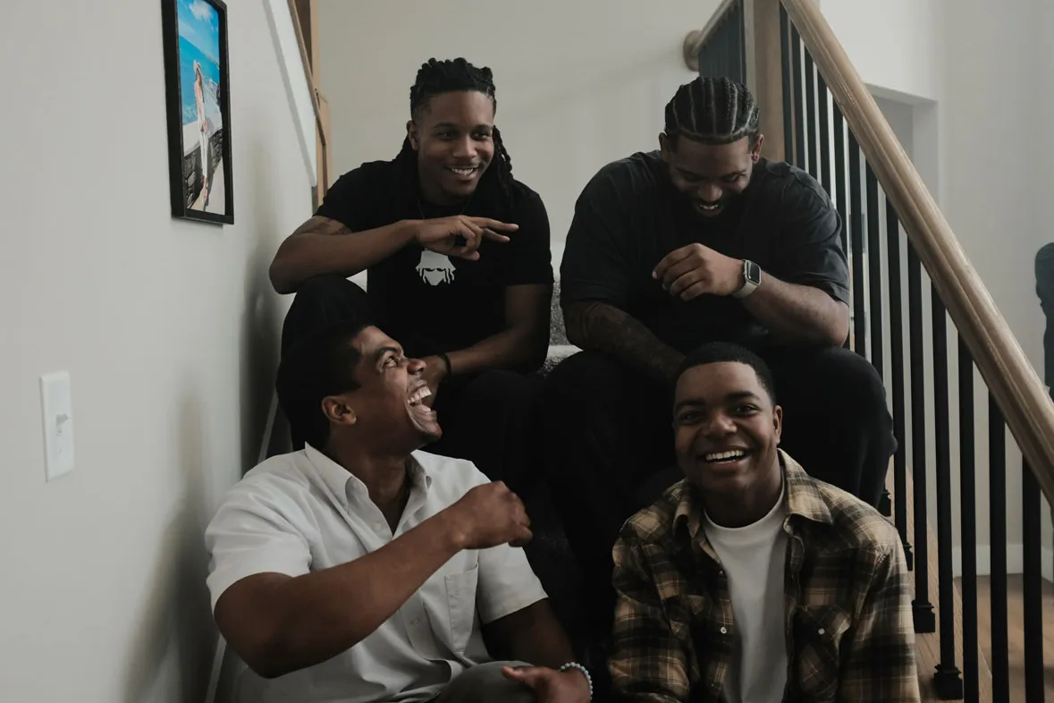 Directors and actors sit on stairs in a filming location that looks to be someone's home. They're genuinely laughing—you can tell they enjoy each other's company and respect one another.